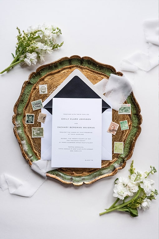 Wedding invitation on a plate with stamps and flowers surrounding it