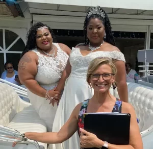 Wedding by Bretta two women LGBTQ in white dresses with a officiant holding a book in front of them