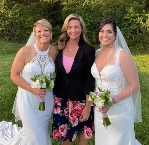 Wedding officiant Indianapolis LGBTQ Bretta in a black suite with pink flowers next to two women in white dresses holding flowers