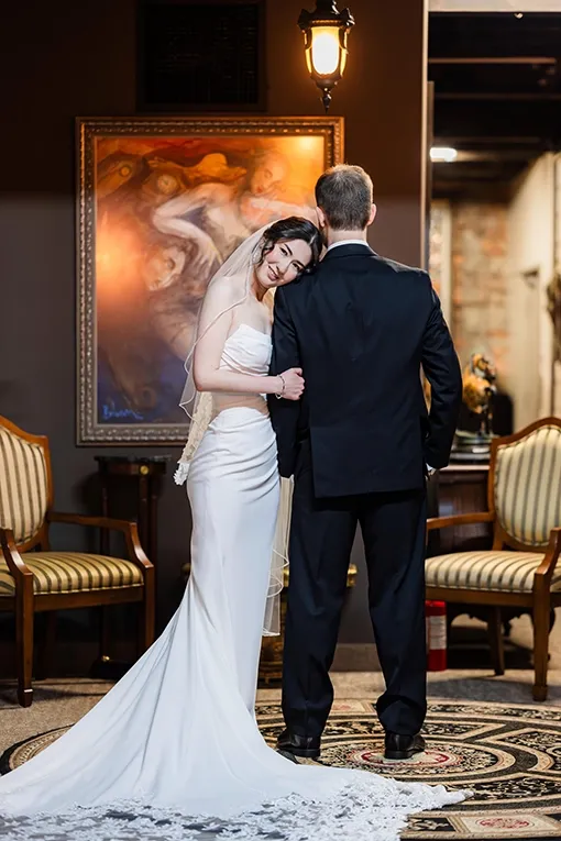 Bride in a white gown and veil smiling and leaning into her groom during an intimate micro wedding ceremony in an elegantly decorated venue Bride in a white gown and veil smiling and leaning into her groom during an intimate micro wedding ceremony in an elegantly decorated venue